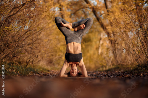 Young woman practicing yoga exercise at autumn park with yellow leaves. Sports and recreation lifestyle