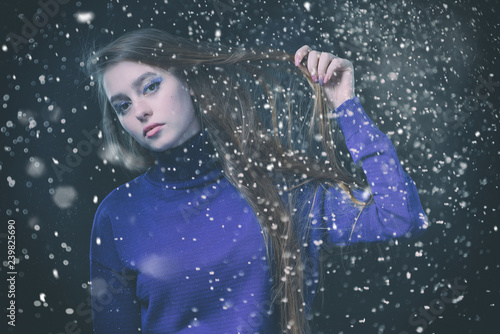 Beautiful, young girl with blond hair in a blue sweater on a snowfall in winter