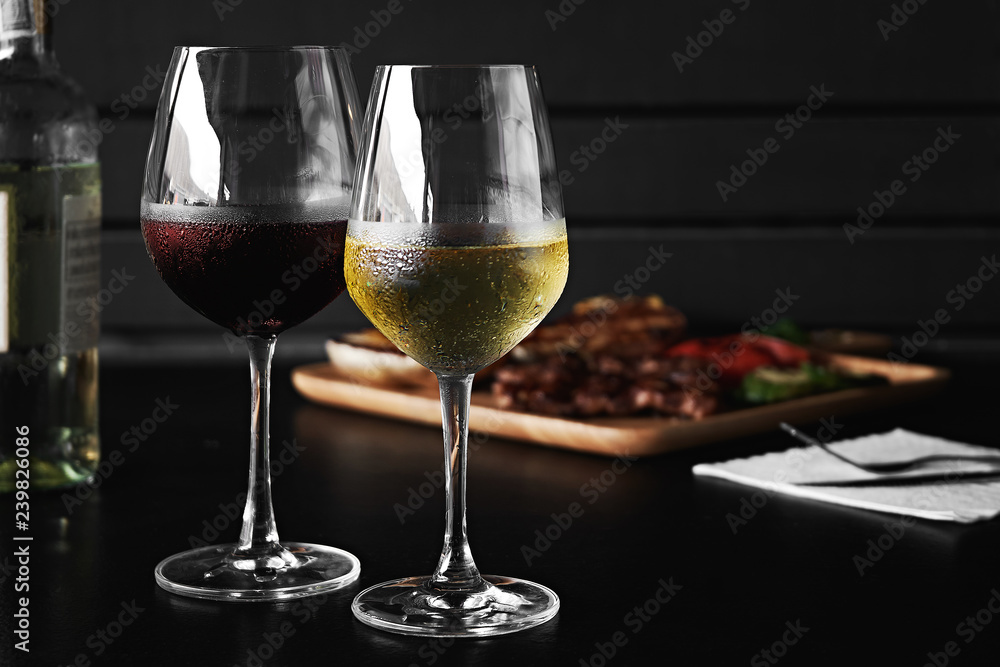 White and red wine pouring in glasses on wooden background