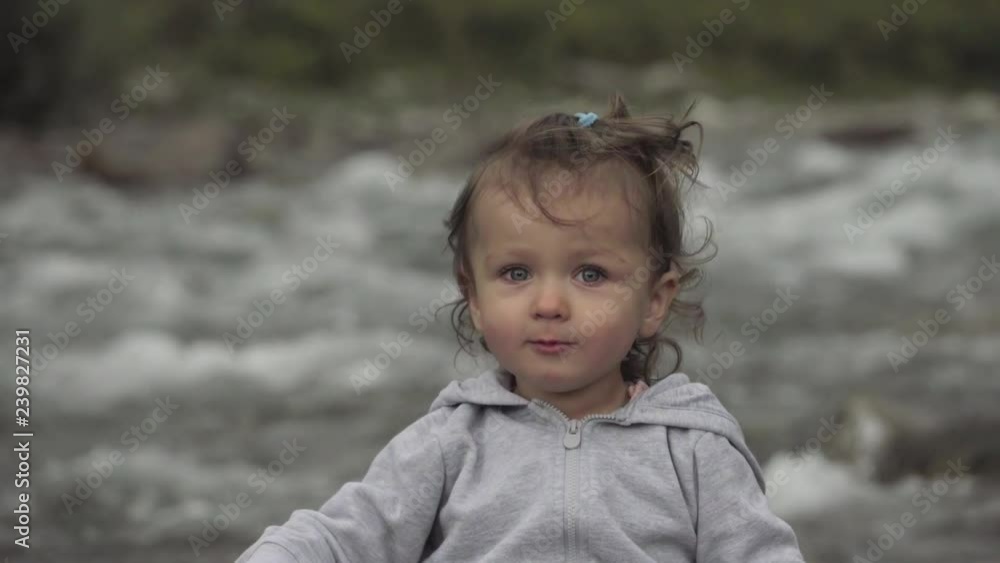 Little girl sits and plays with stick near to river Little girl sits and plays with stick near to river