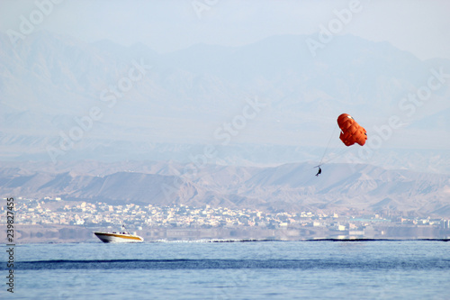 orange paraglider with a cheerful pattern hanging over a boat