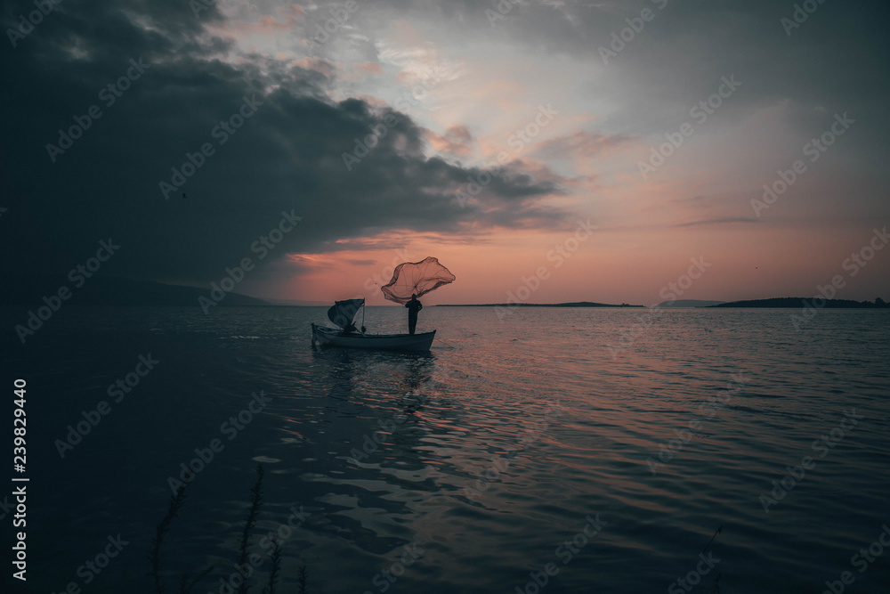 Fototapeta premium A fisherman tries to catch fish in sunset