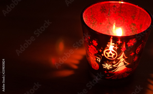 Christmas candle holder alight with a holdiay red glow, depicts scenes of winter and snow by the flame within. photo