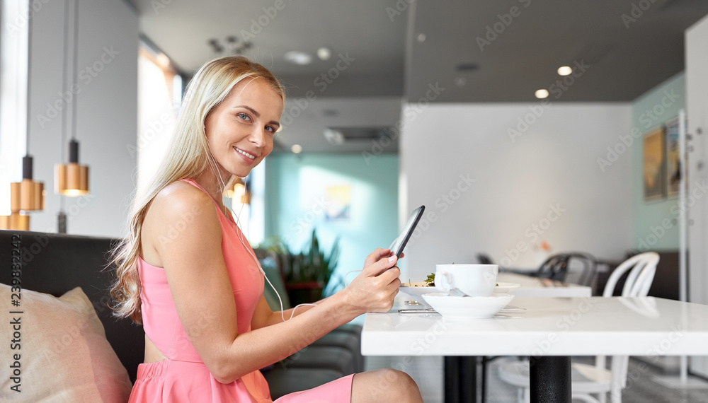 eating, technology, people and leisure concept - happy young woman with tablet pc computer, earphones and food at restaurant