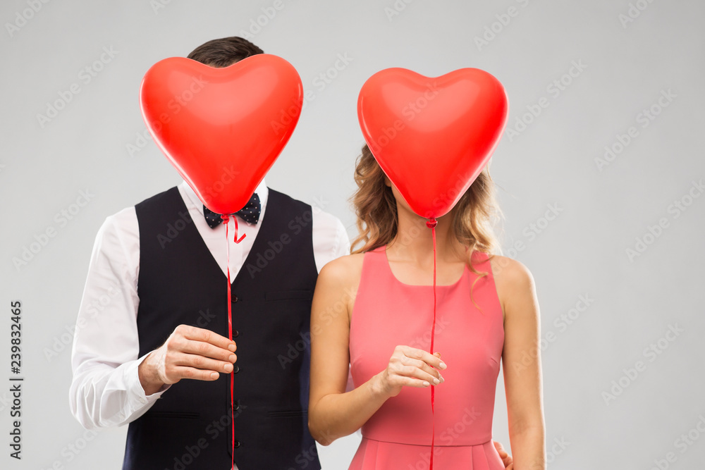 valentines day, love and people concept - couple hiding their faces behind red heart shaped balloons over grey background valentines day, love and people concept - couple hiding their faces behind red heart shaped balloons over grey background