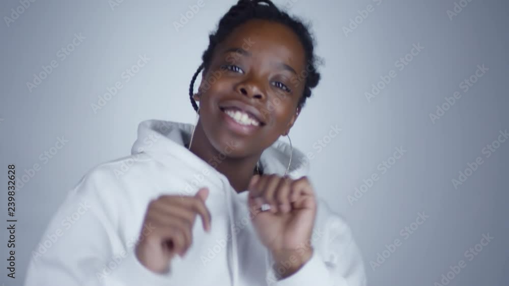 Portrait shot of joyous black woman wearing hoops earrings and white hoodie dancing before camera Portrait shot of joyous black woman wearing hoops earrings and white hoodie dancing before camera