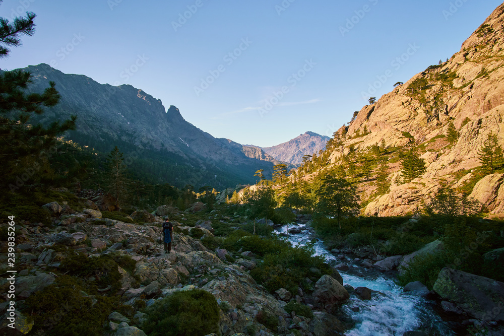 A tourist on a hike in a high altitude alpine valley with a cold stream river in Corsica France mountains GR20