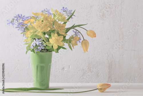 yellow and blue flowers in vase on background old white wall photo