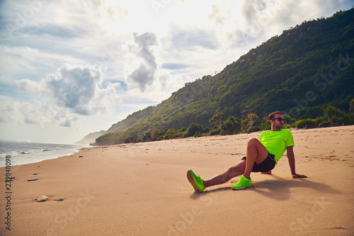 Sportsman stretching on a exotic tropical beach after jogging / exercising.
