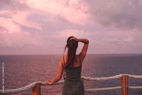 Woman enjoying beautiful colorful sunset above sea from cape