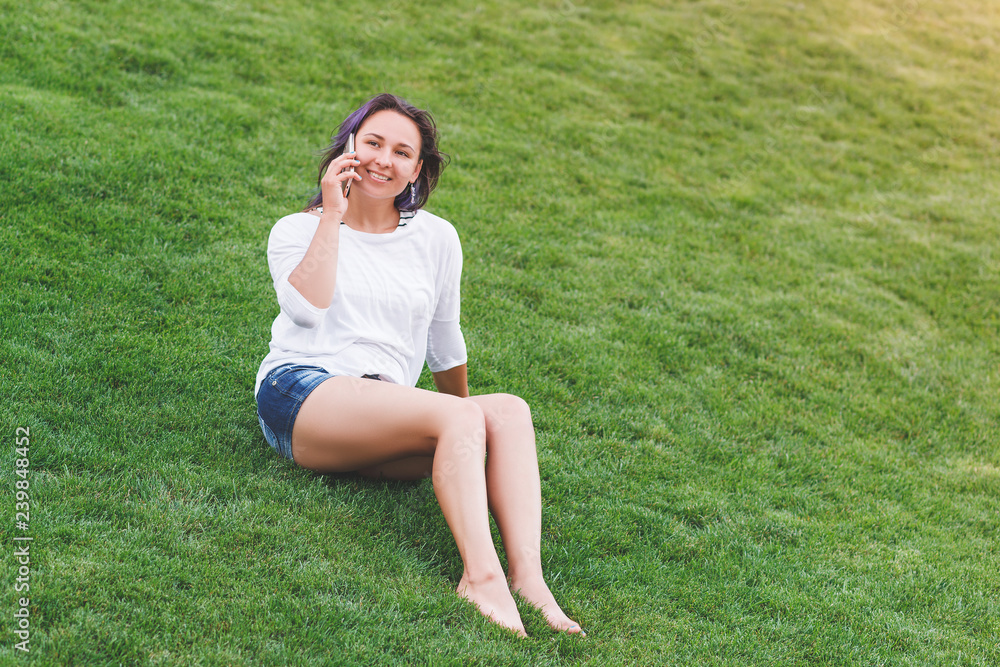 Happy beautiful young woman sitting on grass and using smartphone Happy beautiful young woman sitting on grass and using smartphone