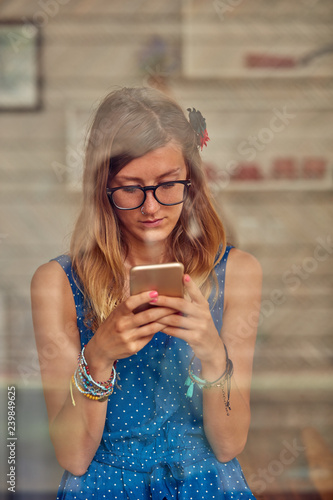 Young woman using smart phone indoors. Window reflection from outdoors.