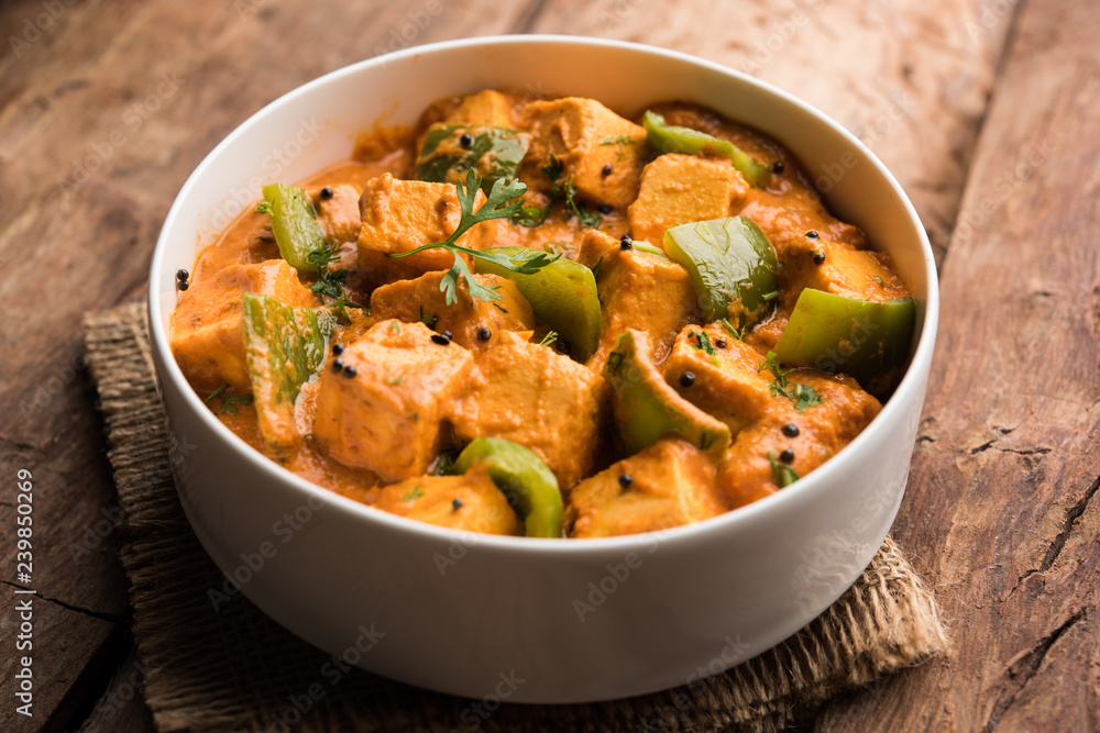 Malai or achari Paneer in a gravy made using red gravy and green capsicum. served in a bowl. selective focus