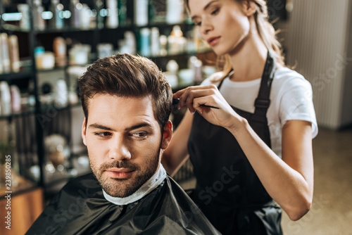 young female hairdresser combing hair to handsome male client in beauty salon