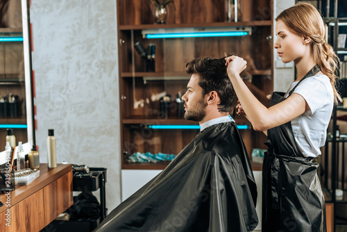 side view of hairstylist cutting hair to handsome young man in beauty salon