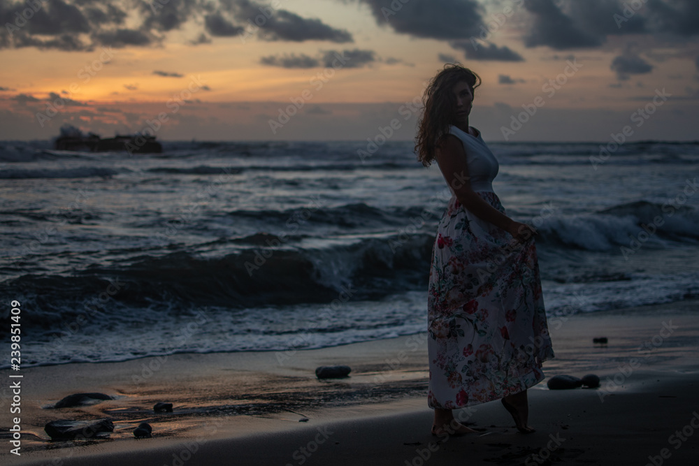 Young dresses woman standing on beach in ocean at sunset Young dresses woman standing on beach in ocean at sunset