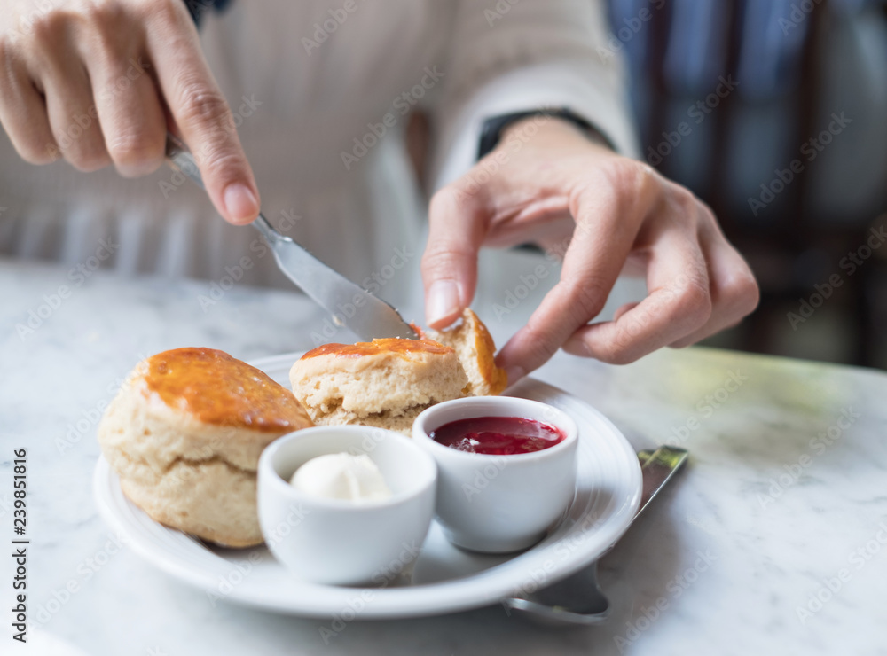 closeup hand of lady is cutting scone with jam
