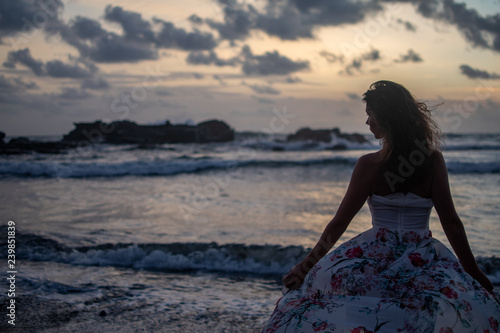 Young dresses woman standing on beach in ocean at sunset