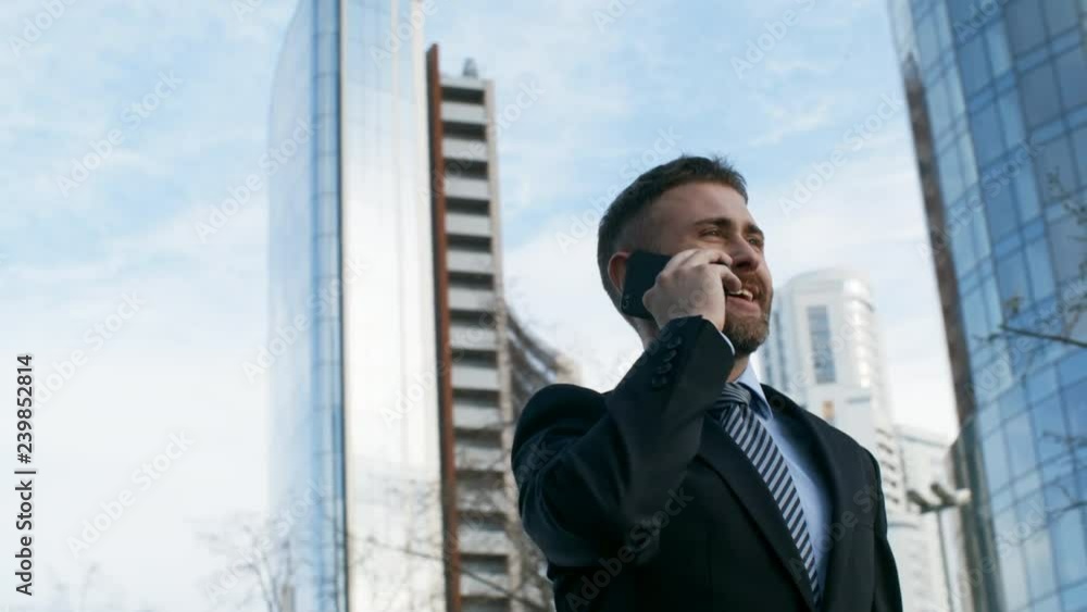 Low angle pan shot of young businessman talking on phone outdoors Low angle pan shot of young businessman talking on phone outdoors