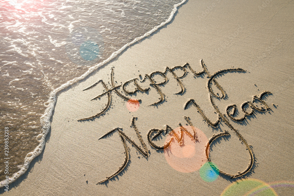 Happy New Year message handwritten in smooth sand with sunrise lens