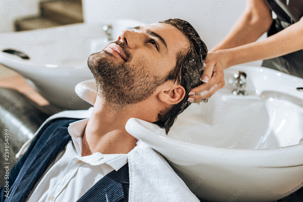 partial view of hairstylist washing hair to handsome smiling man in beauty salon partial view of hairstylist washing hair to handsome smiling man in beauty salon