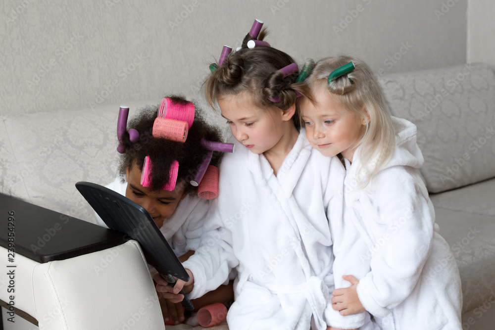 Three girls look at themselves in the mirror. Girls friends in white coats admire enjoying their beauty in the mirror. Three girls look at themselves in the mirror. Girls friends in white coats admire enjoying their beauty in the mirror.