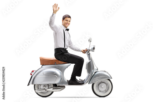 Full length shot of a cheerful young man in smart clothes riding a vintage scooter and waving