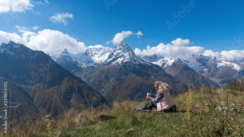 woman traveler drinks coffee with a view of the mountain landscape. A young tourist woman drinks a hot drink from a cup and enjoys the scenery in the mountains. Trekking concept.