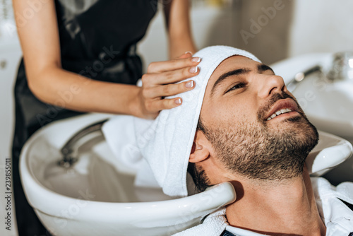 partial view of hairdresser washing hair to smiling handsome man in beauty salon