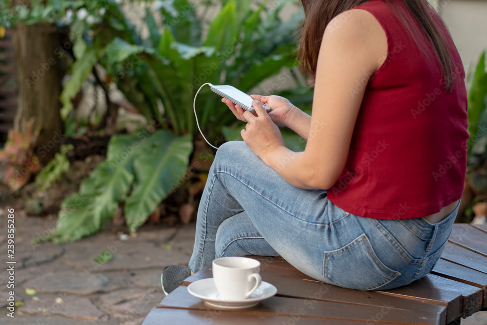 young woman uses smartphone holding it in her hand to listen music from her phone while drinking coffee in the garden young woman uses smartphone holding it in her hand to listen music from her phone while drinking coffee in the garden