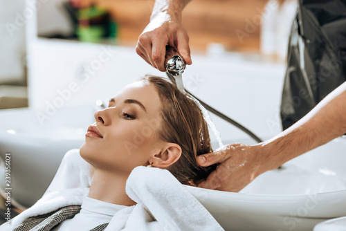 partial view of hairstylist washing hair to attractive young woman in beauty salon photo