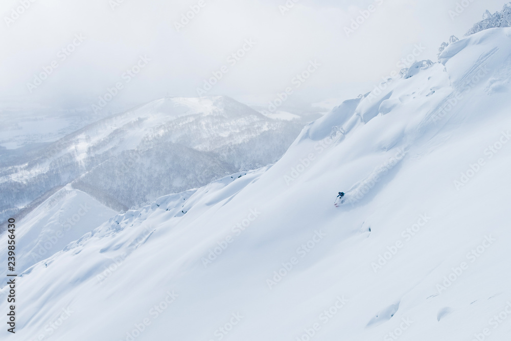 AERIAL: Man shredding the snowy mountain terrain while on fun ski trip in Japan.