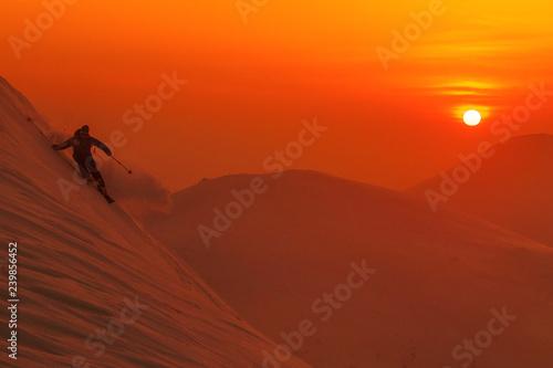 SILHOUETTE: Spectacular shot of pro skier riding off trail on a sunny evening. © helivideo