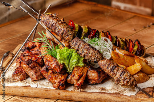 The concept of Georgian cuisine. Meat board with shashlik, grilled pork ribs, lulya kebab and shish kebab. Grilled french fries and grilled vegetables. Meat feed on a wooden board. photo