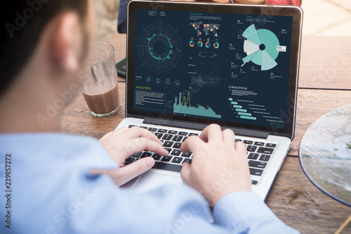 Back view of businessman using laptop with project statistics data, analyzing financial graphs and charts showing company growth on screen.