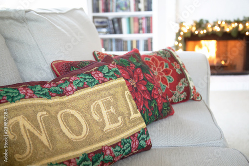 Christmas photograph of Christmas pillows lined up on a couch in front of the fireplace with focus on the word Noel