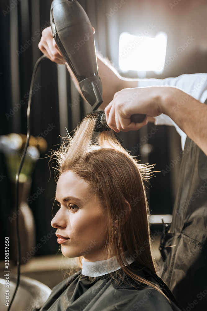 Fototapeta premium Cropped shot of hairstylist drying hair to beautiful young woman in beauty salon
