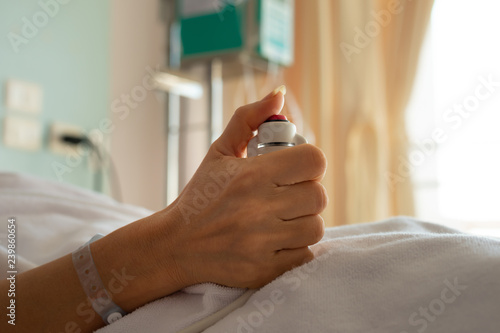 Hand holding nurse call button,selective focused..Woman patient in hospital dress under white blanket holding red emergency call button while lying in bed.