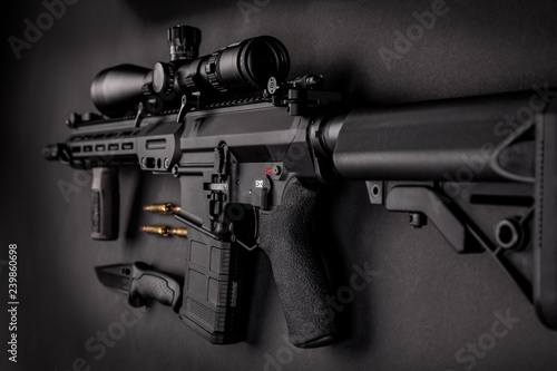 modern automatic rifle with an optical sight lies on a dark background and next to the knife and ammunition