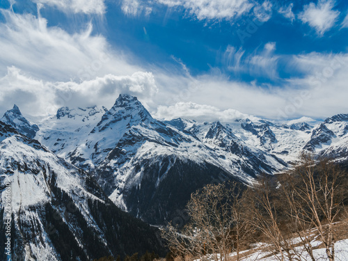 Mountain peaks covered with snow. Sunny day in the snowy mountains. Clouds above the mountain tops. Beautiful mountain background