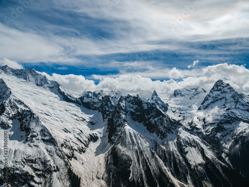 Mountain peaks covered with snow. Sunny day in the snowy mountains. Clouds above the mountain tops. Beautiful mountain background