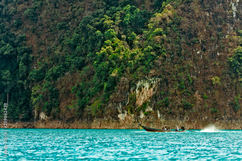 Thai traditional motor boat carries passengers on a mountain lake in Thailand. Jungle in the mountains of Khao SOK national Park. Lake Cheo Lan Thai traditional motor boat carries passengers on a mountain lake in Thailand. Jungle in the mountains of Khao SOK national Park. Lake Cheo Lan