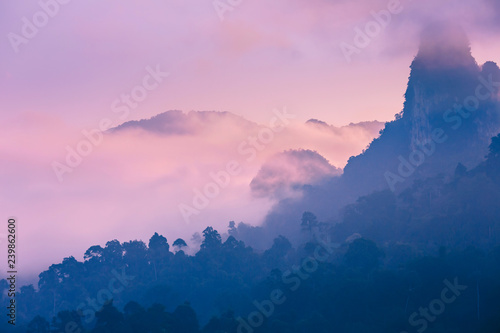 Pink dawn in the exotic mountains of Asia. Dawn on the lake in Thailand. The jungle covers the mountain peaks. Clouds float over the mountains.