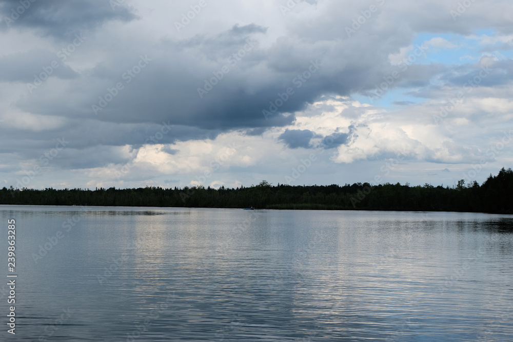 A lake on an overcast cloudy day with a peek through the clouds into the blue sky.