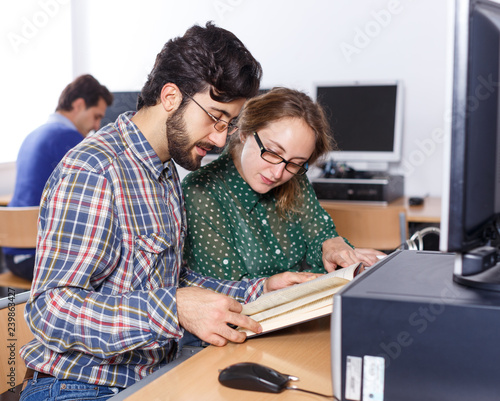 Young people reading book and using pc in library