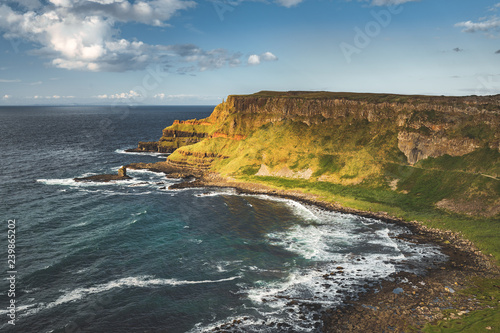 View from above the Northern Ireland shoreline. Ocean water surface next to the grass covered land. Steep cliffs surrounding the cozy bay. Amazing Irish landscape. Beauty of wild virgin nature.