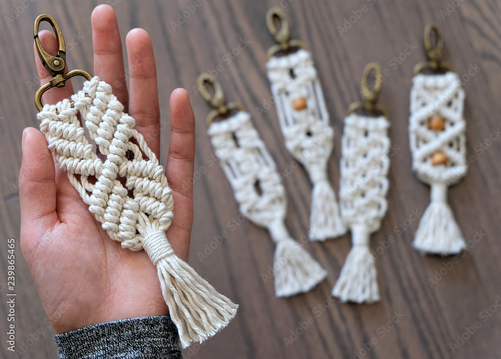 Hand made cotton macrame key chain close up with four blurred in the background that have different styles and some have beads. The background is a beautiful wooden floor. - obrazy, fototapety, plakaty 