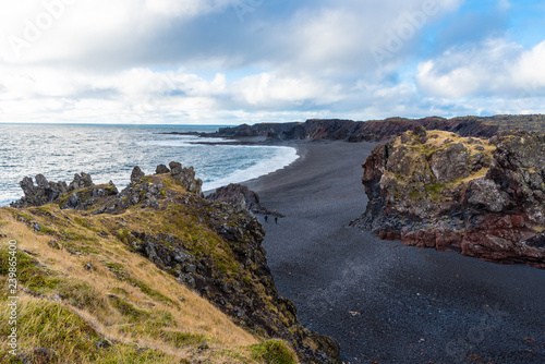 Scenic Black Beach as seen from the Edge of a Cliff in Iceland on a Cloudy Autumn Day. Two People on the Beach are Walking towards the Ocean