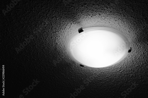 A Black And White Ceiling Light With Popcorn Ceiling Texture That Is Bright Around It And Dark Further Away. photo