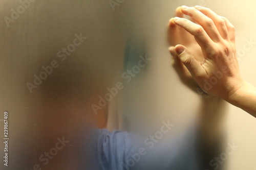A meditative man with a blue bathrobe in a bathroom watching himself in a foggy blurry mirror and resting his hand on it, in an introspective moment